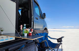 Experience van life! This RV rental offers an outdoor setup with drinks, plants & chair on a bright white salt flat. Perfect for travel.