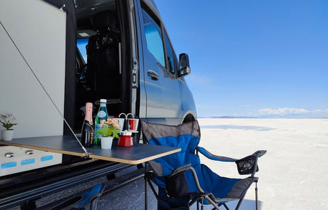 Experience van life! This RV rental offers an outdoor setup with drinks, plants & chair on a bright white salt flat. Perfect for travel.