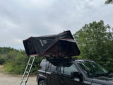 Black Jeep Patriot SUV with a deployed rooftop tent and ladder