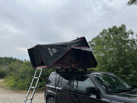 Black Jeep Patriot SUV with a deployed rooftop tent and ladder