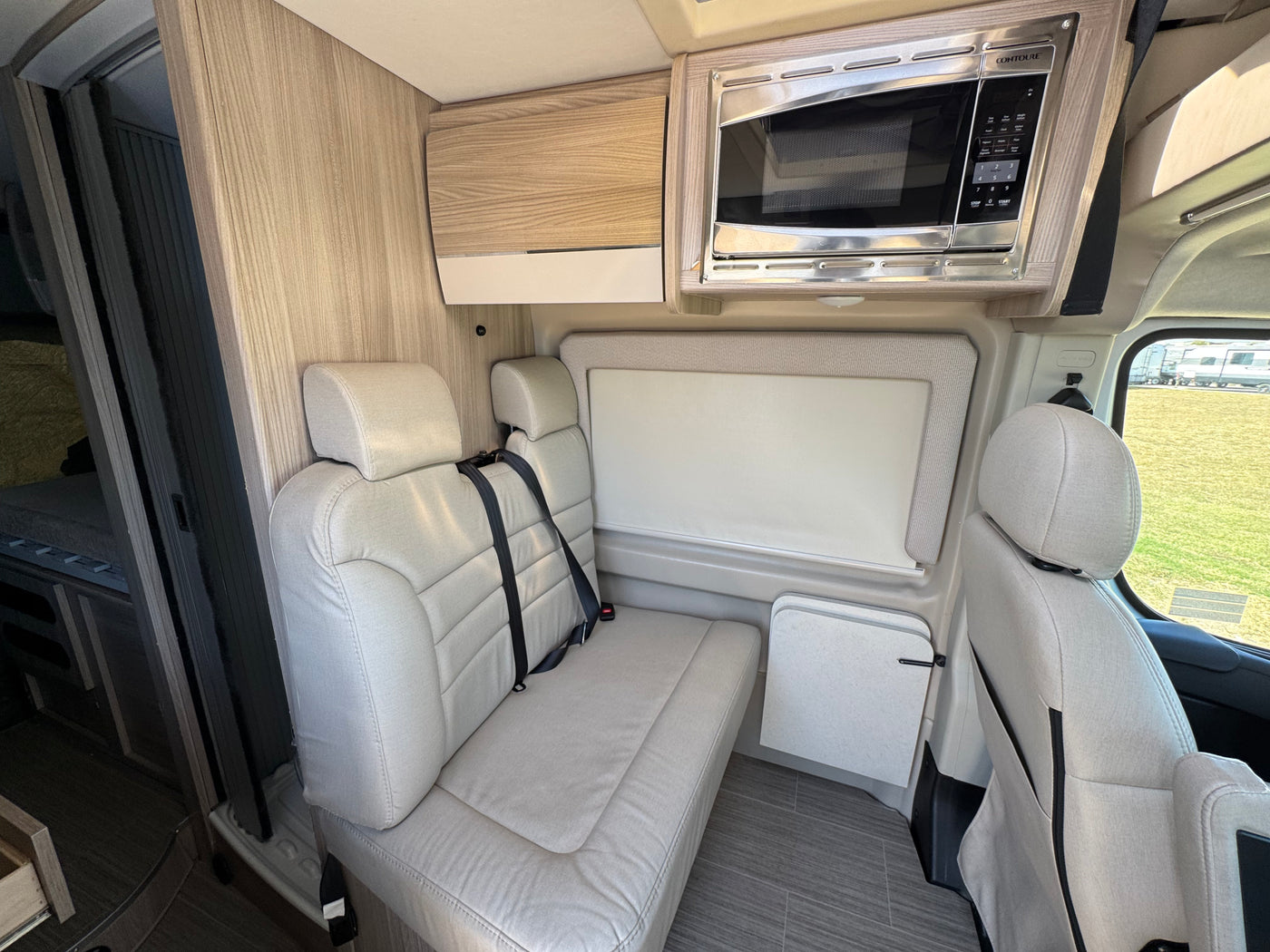 RV rental interior featuring comfortable passenger seating with seatbelts, a microwave, and a fold-down table for travel. — photo 5