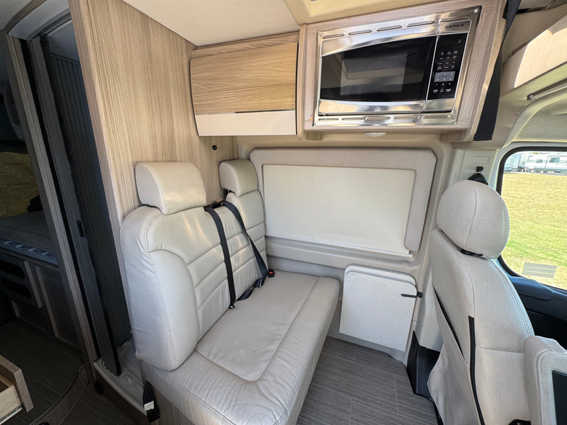 RV rental interior featuring comfortable passenger seating with seatbelts, a microwave, and a fold-down table for travel. — photo 5
