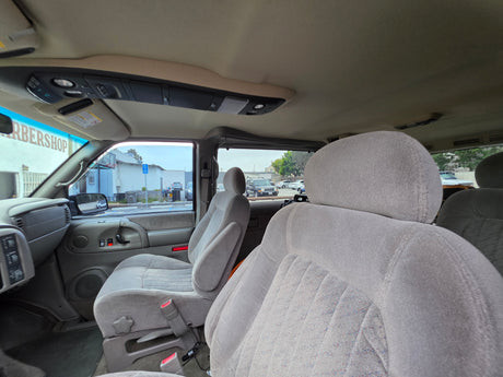 Inside an RV rental van: light grey fabric seats, overhead console, and view of a barbershop outside.