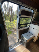 Enjoy nature from this RV rental! The camper van's open side door reveals a forest view, with a Dometic fridge inside.