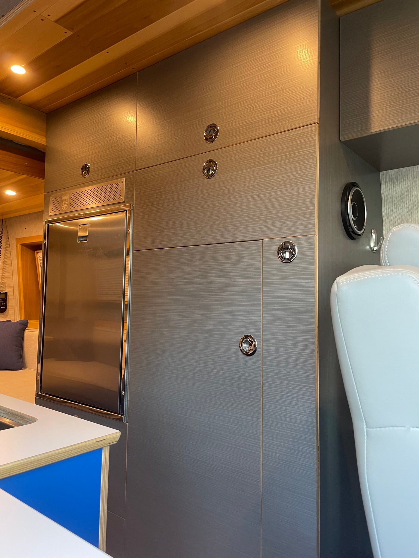 Sleek rv rental interior with stainless steel fridge, modern brushed cabinetry, wooden ceiling, and a white upholstered seat. — photo 16
