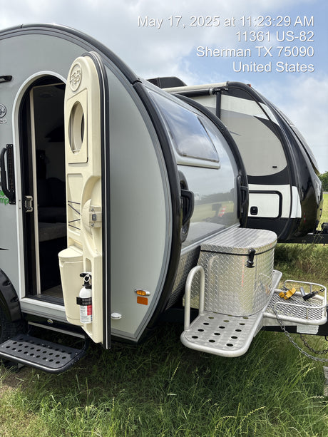 A teardrop travel trailer with an open door, alongside another RV, sitting on grass in Sherman, TX. Explore an RV rental!