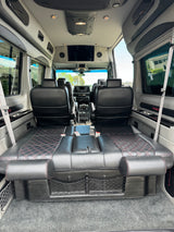 Luxury rv rental interior. Features plush black leather seats with red stitching, TV, and a convertible rear bed for comfortable travel.