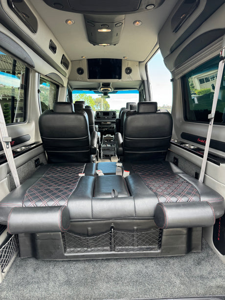 Luxury rv rental interior. Features plush black leather seats with red stitching, TV, and a convertible rear bed for comfortable travel.