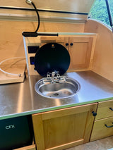Compact **RV rental** kitchen features a stainless steel sink, Dometic cover, CFX cooler, and wooden cabinets.