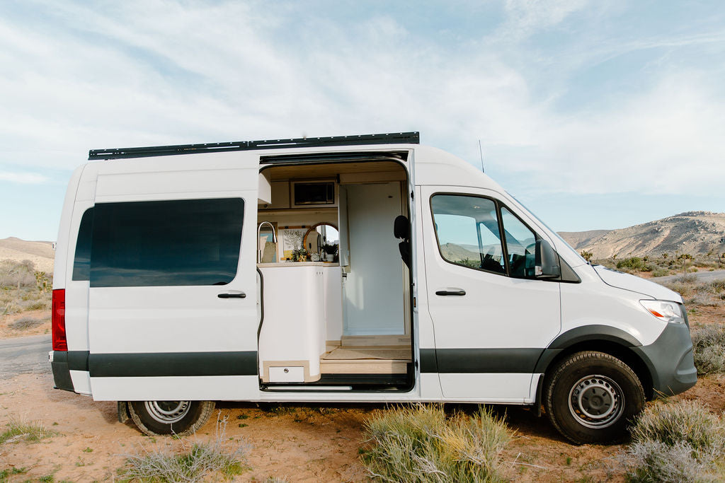 White camper van RV rental parked in desert. Open side door reveals cozy interior with sink. Ready for your next adventure!
