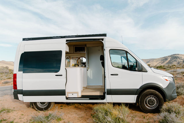 White camper van RV rental parked in desert. Open side door reveals cozy interior with sink. Ready for your next adventure!