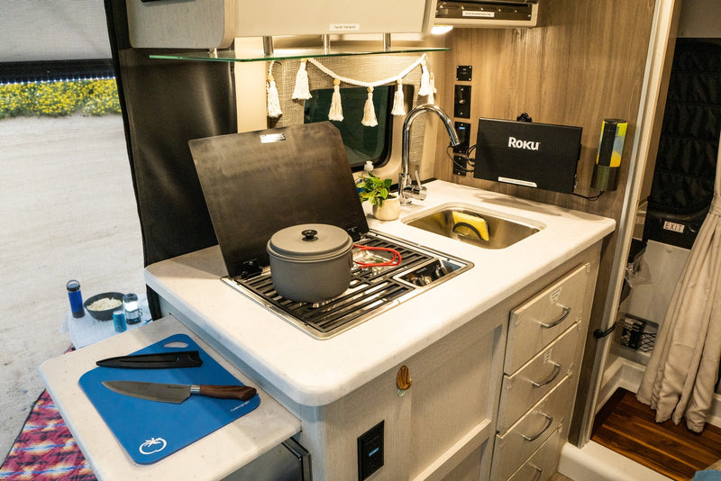 This RV rental features a compact kitchen with a stove, sink, cutting board, and a screened outdoor view. — photo 9