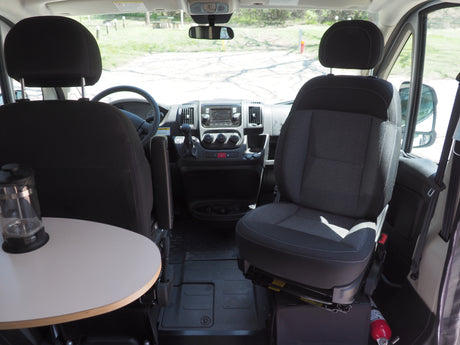 RV rental interior: Front cabin shows swiveling seats, dashboard, small table with French press, and a fire extinguisher.