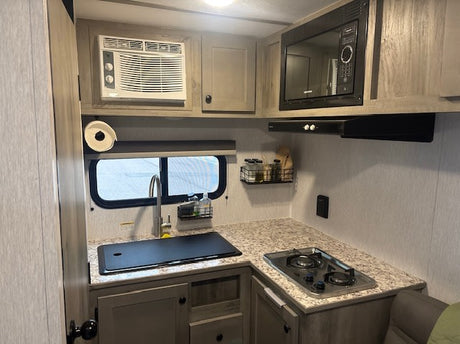  empty two-door refrigerator and freezer with shelves is ready for your food and drinks.|Overhead cabinet in an RV rental with folded blankets for storage. An essential view of practical RV interior organization.|Organized RV rental kitchen cabinet: stacked mugs