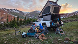 Scenic mountain camping adventure with an RV rental. A group with their dog enjoys a campfire at sunset.