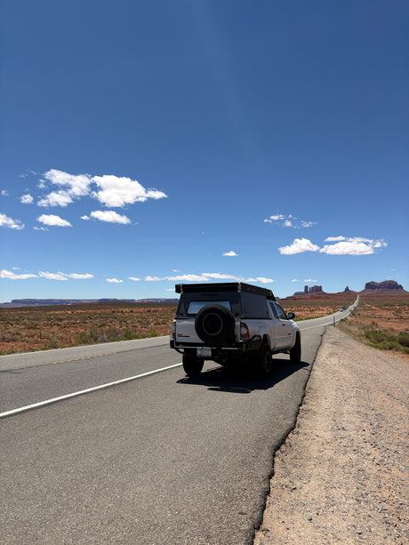 Exploring Monument Valley with an RV rental pickup truck camper on a winding desert road under blue skies.