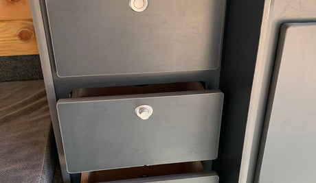 Inside this RV rental, grey storage drawers with push-button latches offer organization. Two are slightly open, revealing wood.