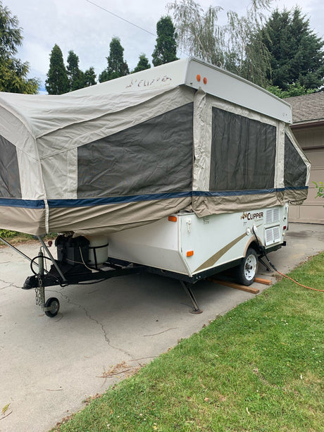 White pop-up camper for RV rental, fully expanded in a driveway, ideal for camping and outdoor adventures.