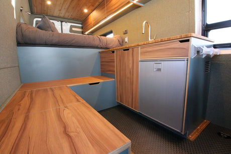 Explore this RV rental's versatile interior, featuring a sleek kitchen with a fridge, comfy bed, and adaptable table.