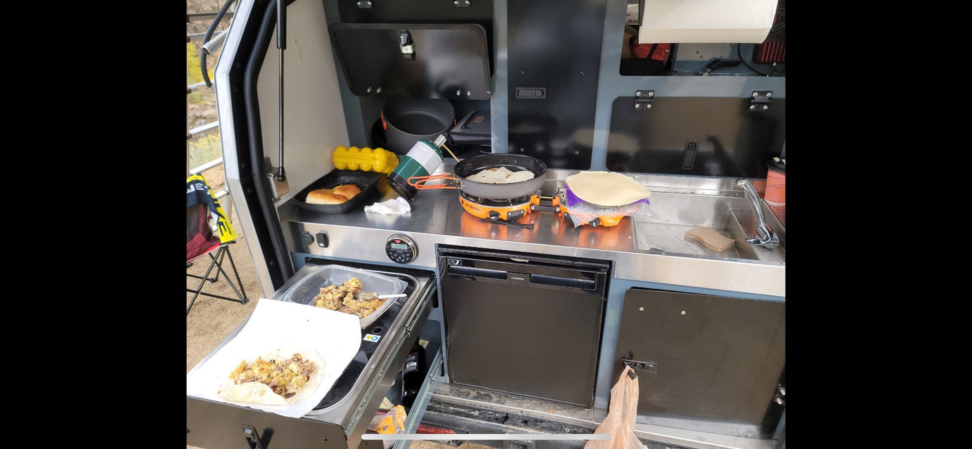 Preparing breakfast in a convenient RV rental outdoor kitchen setup, featuring a portable stove, sink, and fridge.