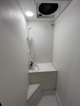 RV rental: A compact, all-white wet bath with shower, overhead fan, and light. Includes a multi-level floor for functionality.