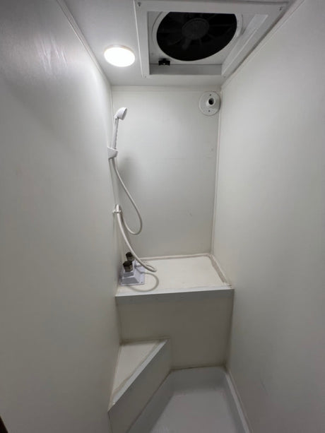 RV rental: A compact, all-white wet bath with shower, overhead fan, and light. Includes a multi-level floor for functionality.
