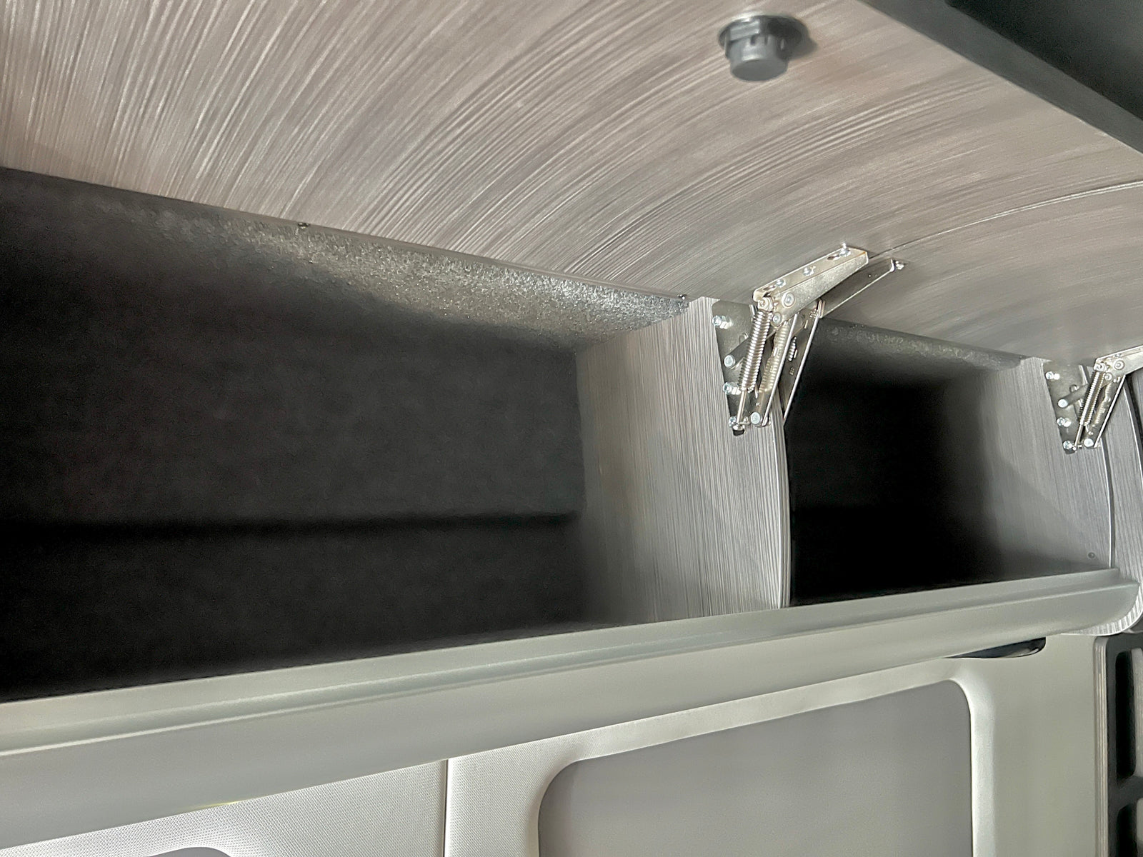 Overhead storage in this RV rental: spacious compartments with light wood-grain texture, dark interiors, and strong spring hinges.