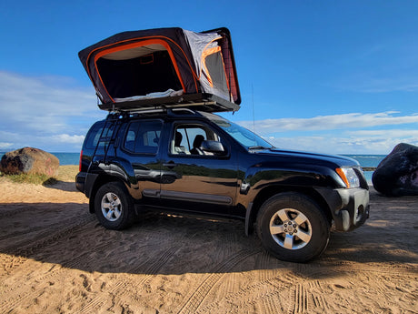 Black SUV with rooftop tent set up on a sandy beach. Perfect for your next beach camping rv rental adventure!