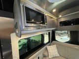 RV rental living space: Stainless steel microwave, wood cabinets, and comfy upholstered seating by the window.