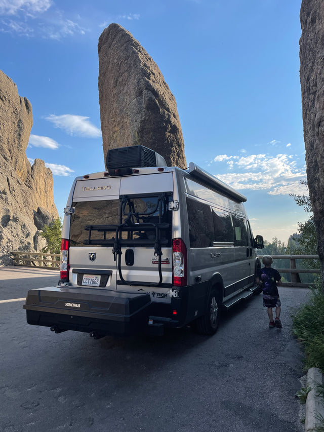 An RV rental camper van parked amidst majestic rock formations. A child stands beside it, enjoying the scenic view.