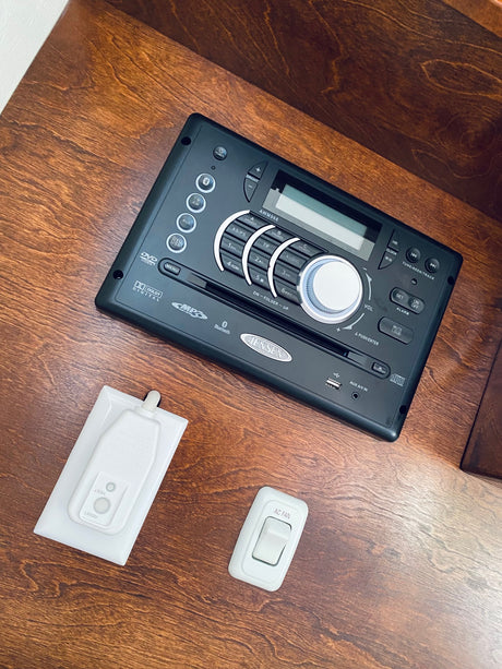 RV rental interior with a Jensen stereo, AC fan switch, and electrical safety device on a wooden surface.