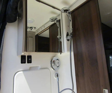 This RV rental bathroom features a compact shower with fixtures, mirror cabinet, and a "WATER PUMP" switch.