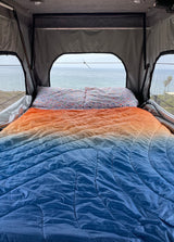 Scenic ocean view from a cozy rv rental bed with an orange & blue comforter. Ideal for relaxing camping trips.