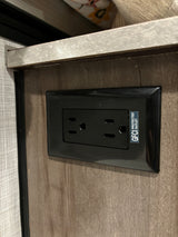 Standard black GFCI protected electrical outlet in an RV rental interior, mounted on a wood-grain panel.