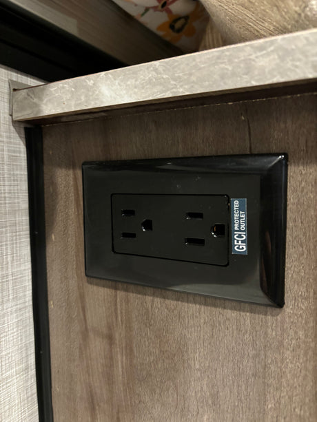 Standard black GFCI protected electrical outlet in an RV rental interior, mounted on a wood-grain panel.