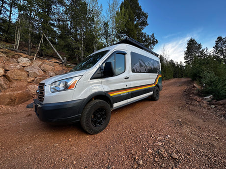 Adventure awaits with this RV rental! A white VANDOIT camper van on a rocky dirt road in a forest, ready for exploration.