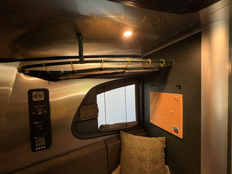 Cozy RV rental interior featuring an upper bunk, control panel, window, and small bulletin board.