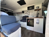 Stylish RV rental interior: cozy seating/bed, complete kitchen with microwave, sink & fridge. Ready for adventure.