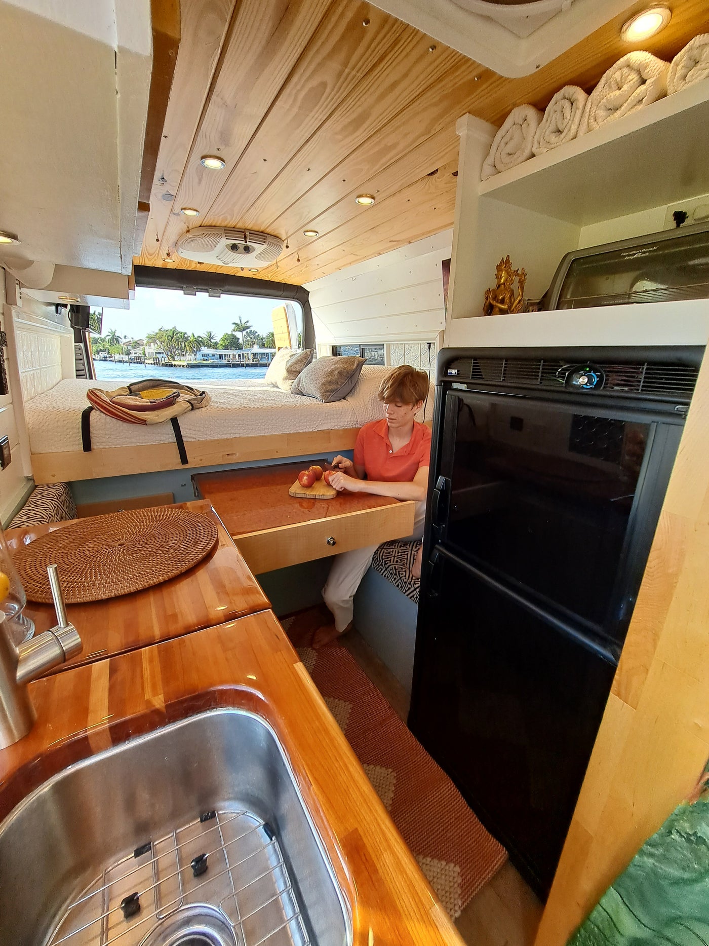 Inside a charming RV rental: A woman chops apples in a wooden camper van kitchen, overlooking a scenic waterfront view. — photo 19