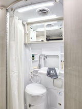 Explore comfort in your RV rental with this fully-equipped compact bathroom, featuring a toilet, sink, and shower.