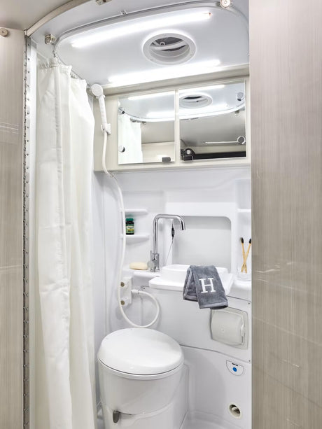 Explore comfort in your RV rental with this fully-equipped compact bathroom, featuring a toilet, sink, and shower.