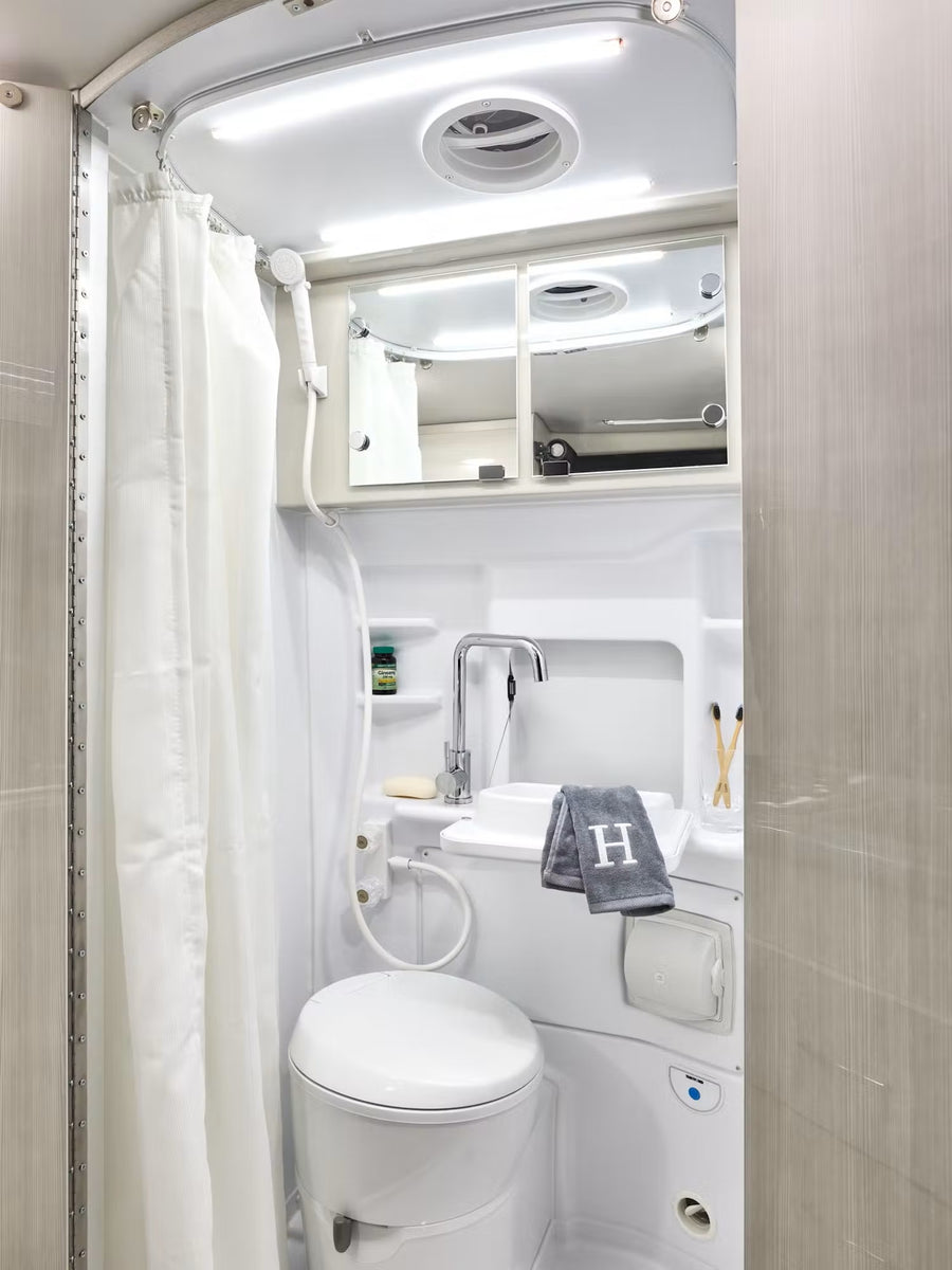 Explore comfort in your RV rental with this fully-equipped compact bathroom, featuring a toilet, sink, and shower.