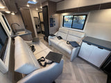 Modern RV rental interior: bright, spacious living area with two white recliners, kitchen, and wood-look flooring.
