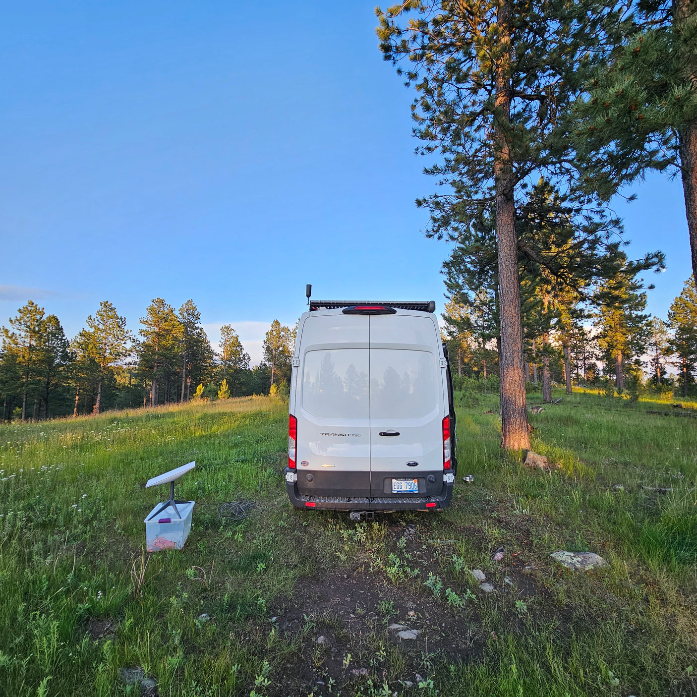 An RV rental (white Ford Transit van) in a peaceful forest with a Starlink dish, offering off-grid connectivity and nature.
