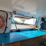 Experience van life! Custom rv rental interior with a vibrant turquoise workspace and scenic outdoor views from the open back doors.
