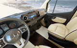 The modern, luxurious interior of a Mercedes-Benz RV with a dashboard, steering wheel, and cream seating, offering a beach view. Ideal for rv rental.