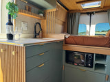 Step into this modern RV rental: a cozy van interior with a well-equipped kitchen, bed, and wooden details.