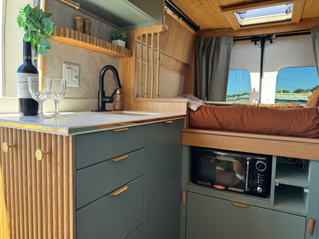 Step into this modern RV rental: a cozy van interior with a well-equipped kitchen, bed, and wooden details.