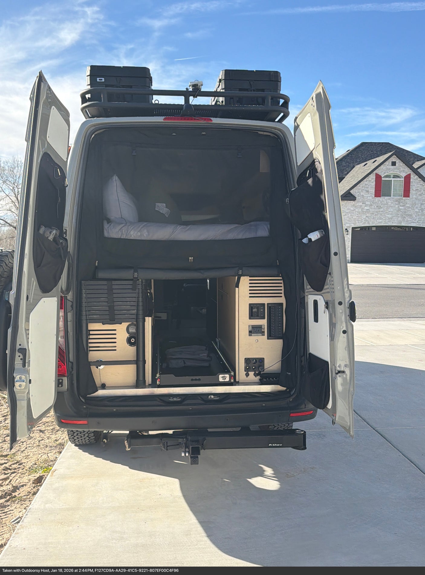 Open rear doors of this custom RV rental reveal a cozy bed, organized storage, and roof-mounted gear, perfect for adventure.
