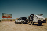 White Jeep towing an XTR off-road RV rental camper in the Utah desert by a welcome sign.